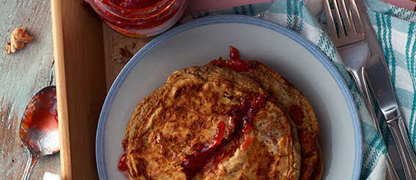 A serving of pancakes resting on a plate ready to eat, with a jar of Jam sitting alongside it.